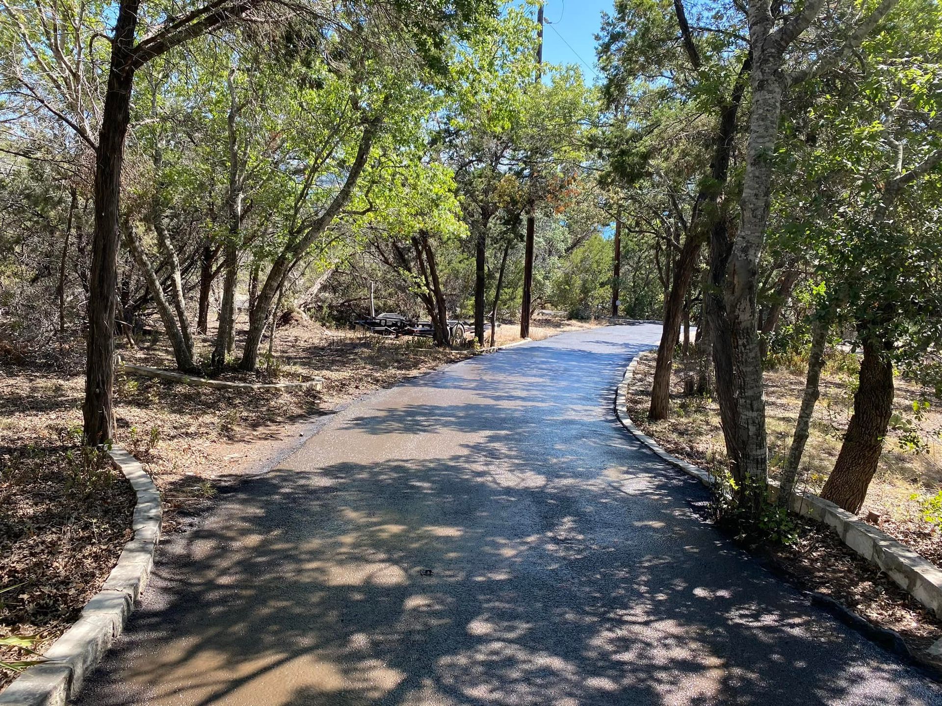 Paved road winding through a wooded area with trees and sunlight.