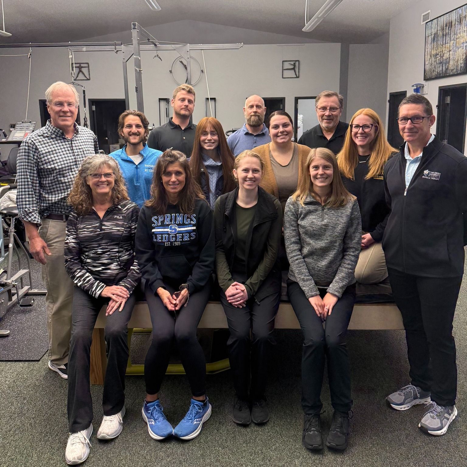 Group of people in a physical therapy clinic, posing for a photo near equipment.
