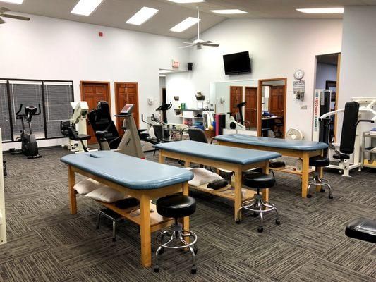 Physical therapy room with treatment tables, exercise equipment, and stools.