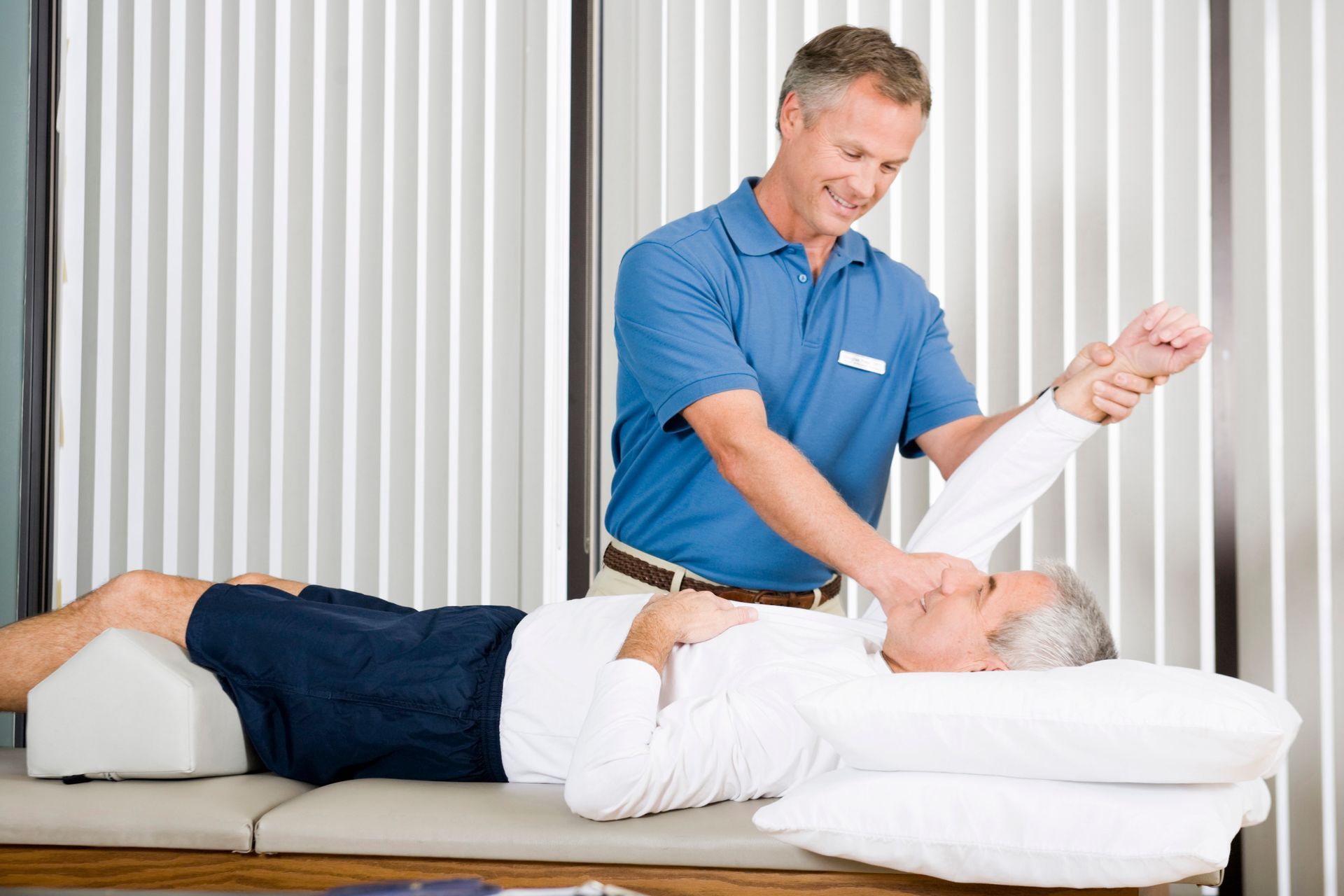 Physical therapist stretches patient's arm while patient lies on treatment table.