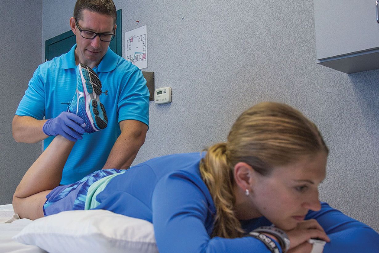 Physical therapist stretching patient's arm; therapy room setting.