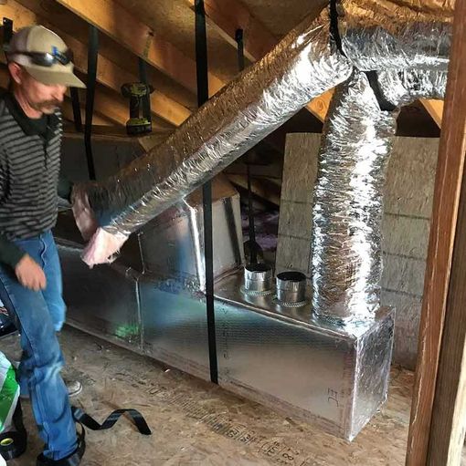 Man installing HVAC ductwork in an attic.