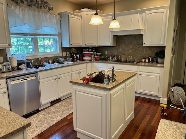 White kitchen with cabinets, island, stainless steel dishwasher, and hardwood floors.