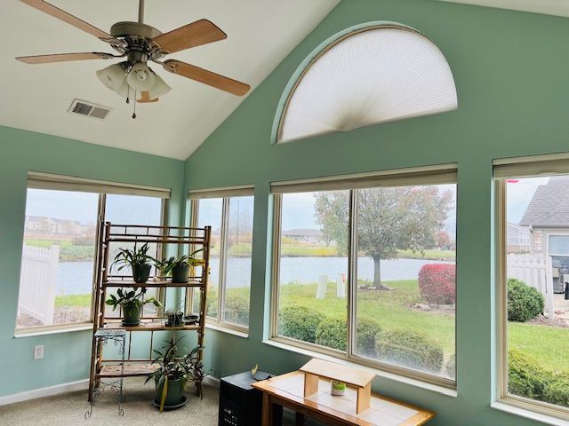 Sunroom with teal walls, large windows overlooking a lake, and a ceiling fan.