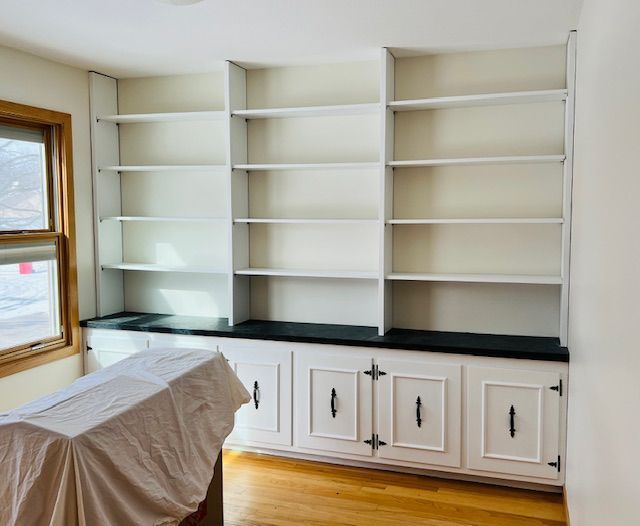 White built-in bookshelves with black countertop and lower cabinets in a room with hardwood floors and a window.