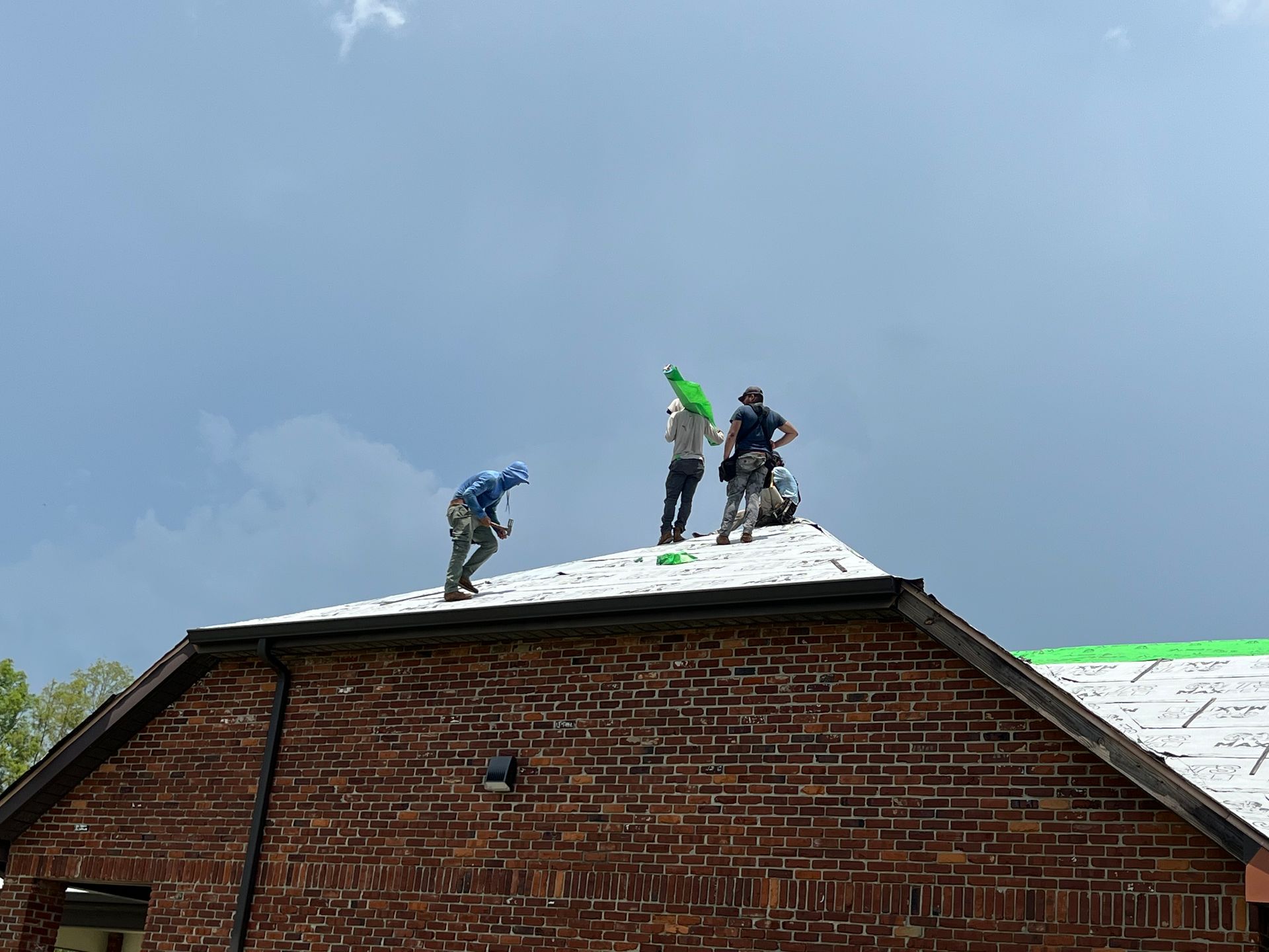 Roofers working on a brick building's roof under a cloudy sky.