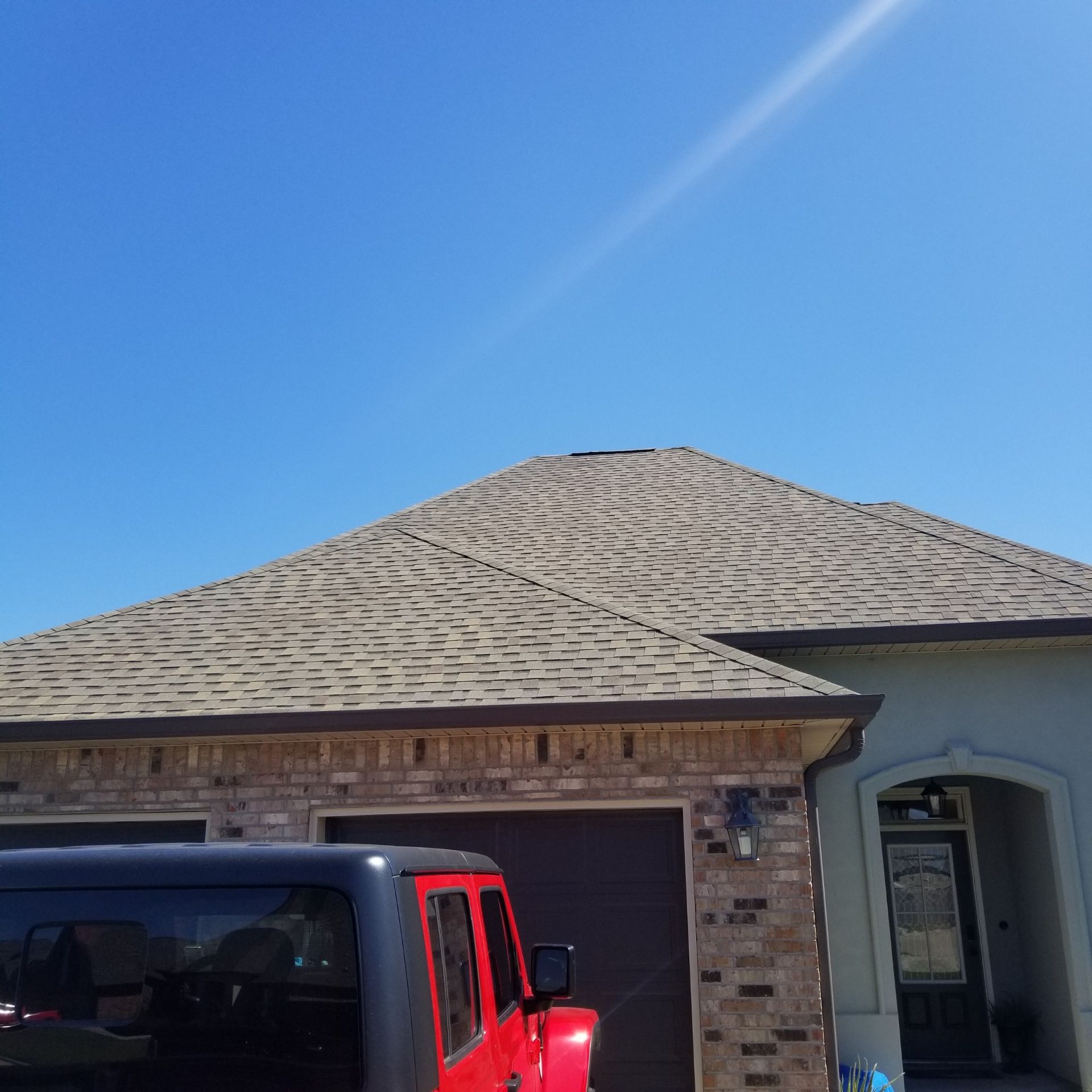 Tan shingled roof on house with a red Jeep parked in front, clear blue sky overhead.