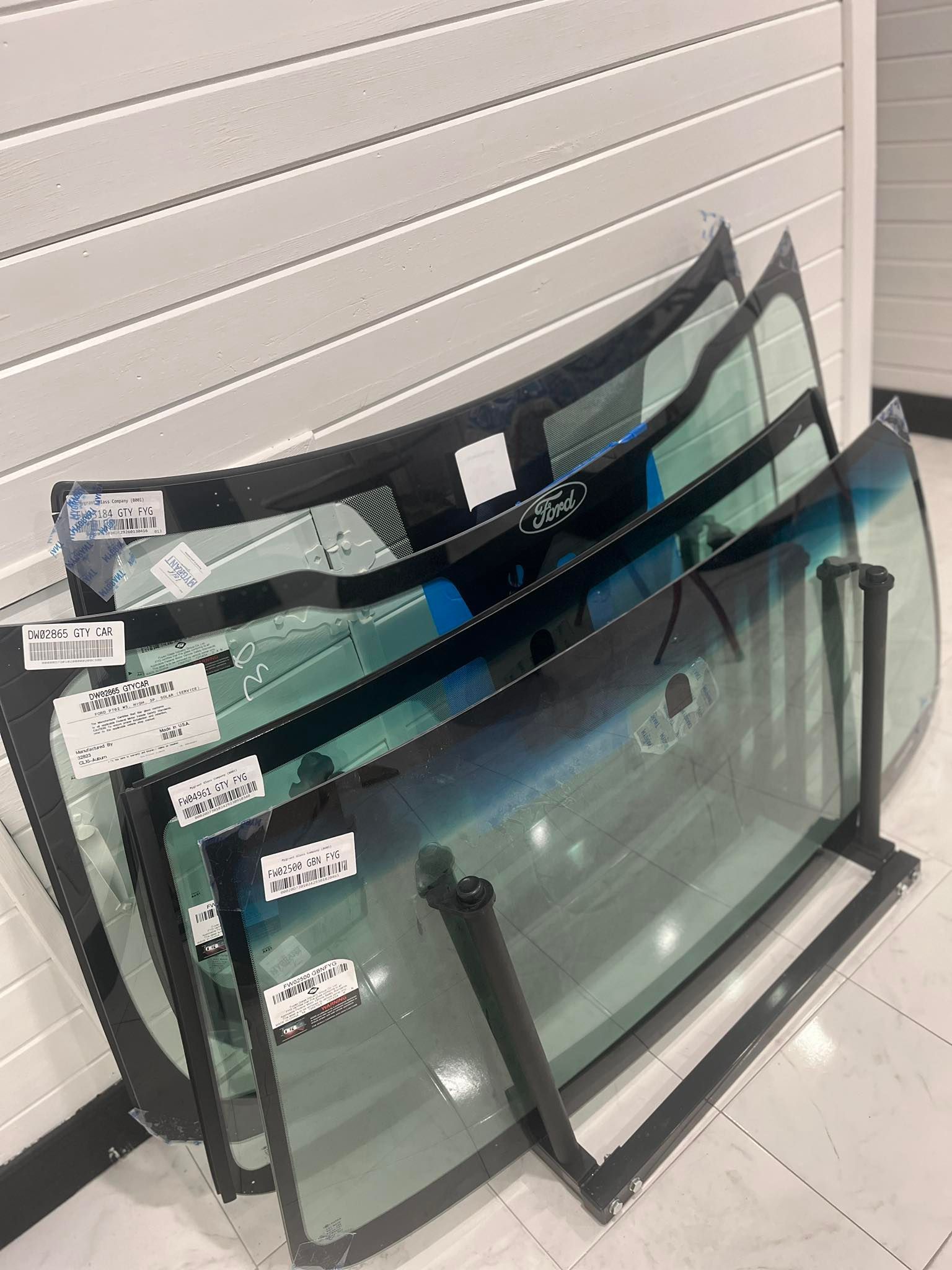 A rack holding several curved automotive windshields in a shop with white paneling.