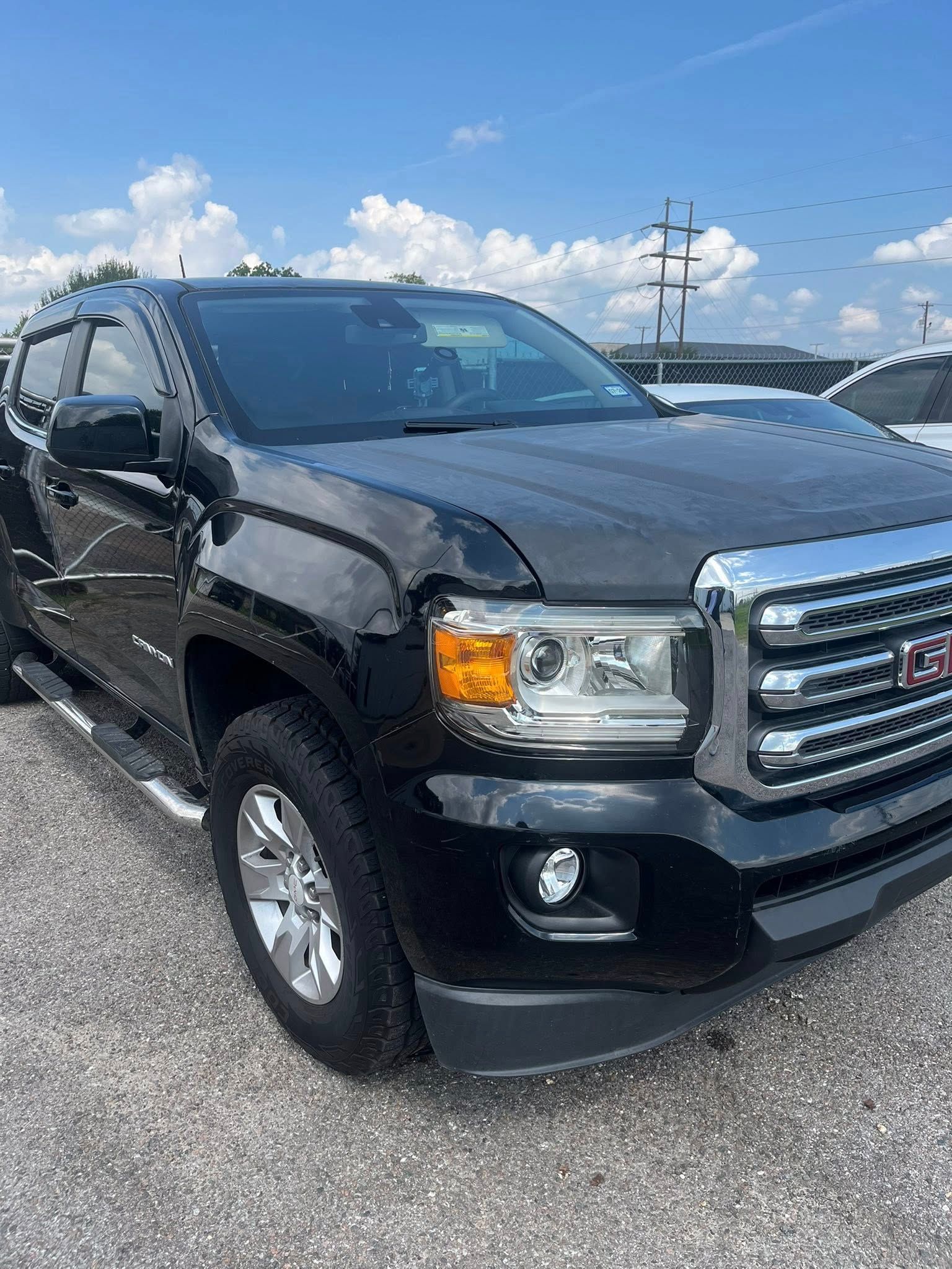 A black GMC Canyon pickup truck parked on a gravel lot under a bright blue sky.