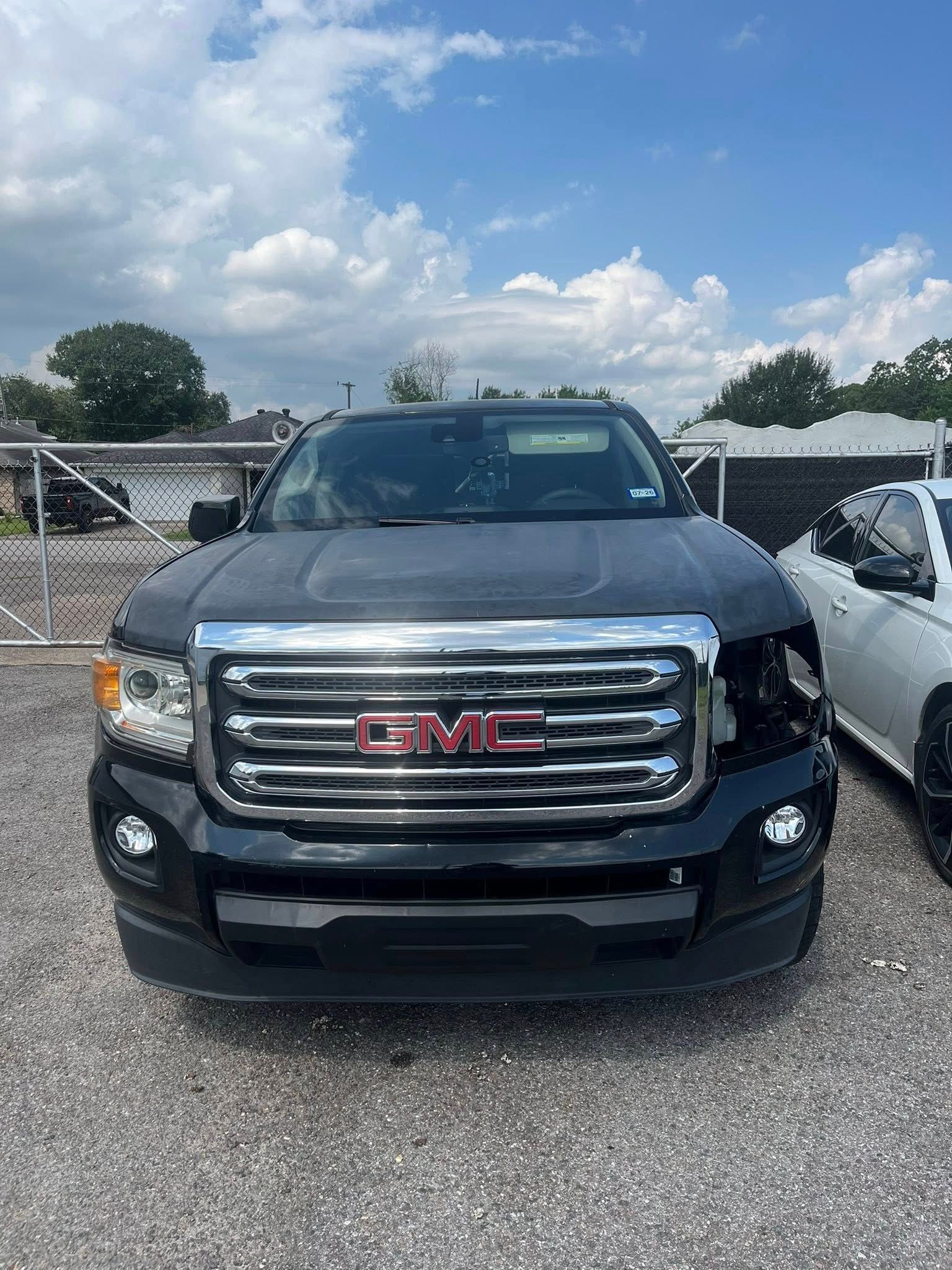 A black GMC pickup truck parked on gravel with a missing driver's side headlight assembly.