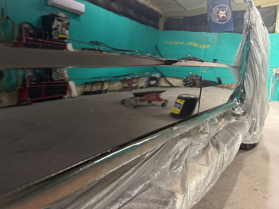 A highly reflective black surface in a shop, showing a mirror image of the garage, tools, and teal walls.