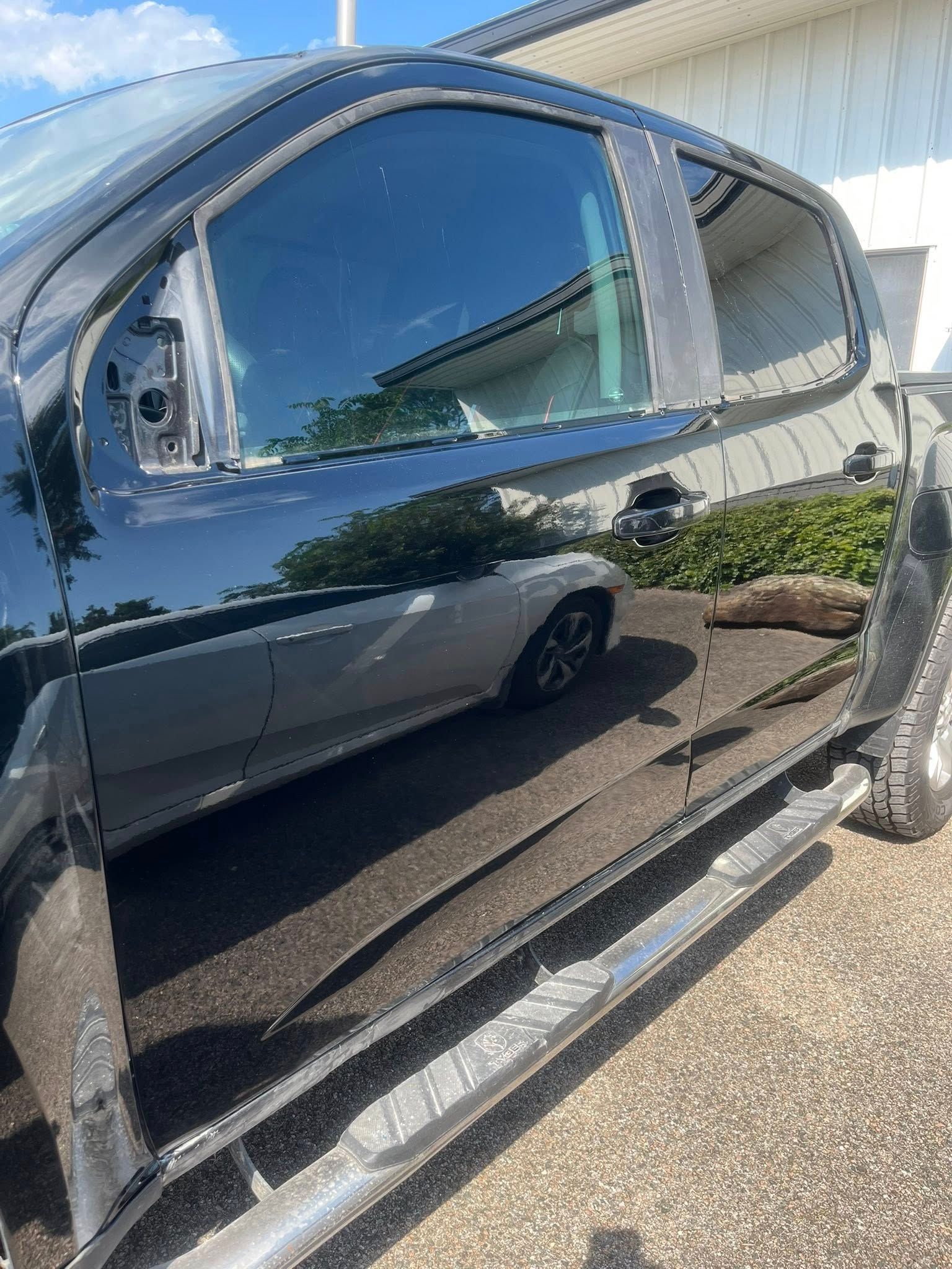 A side view of a black pickup truck with the side mirror missing, parked on asphalt.