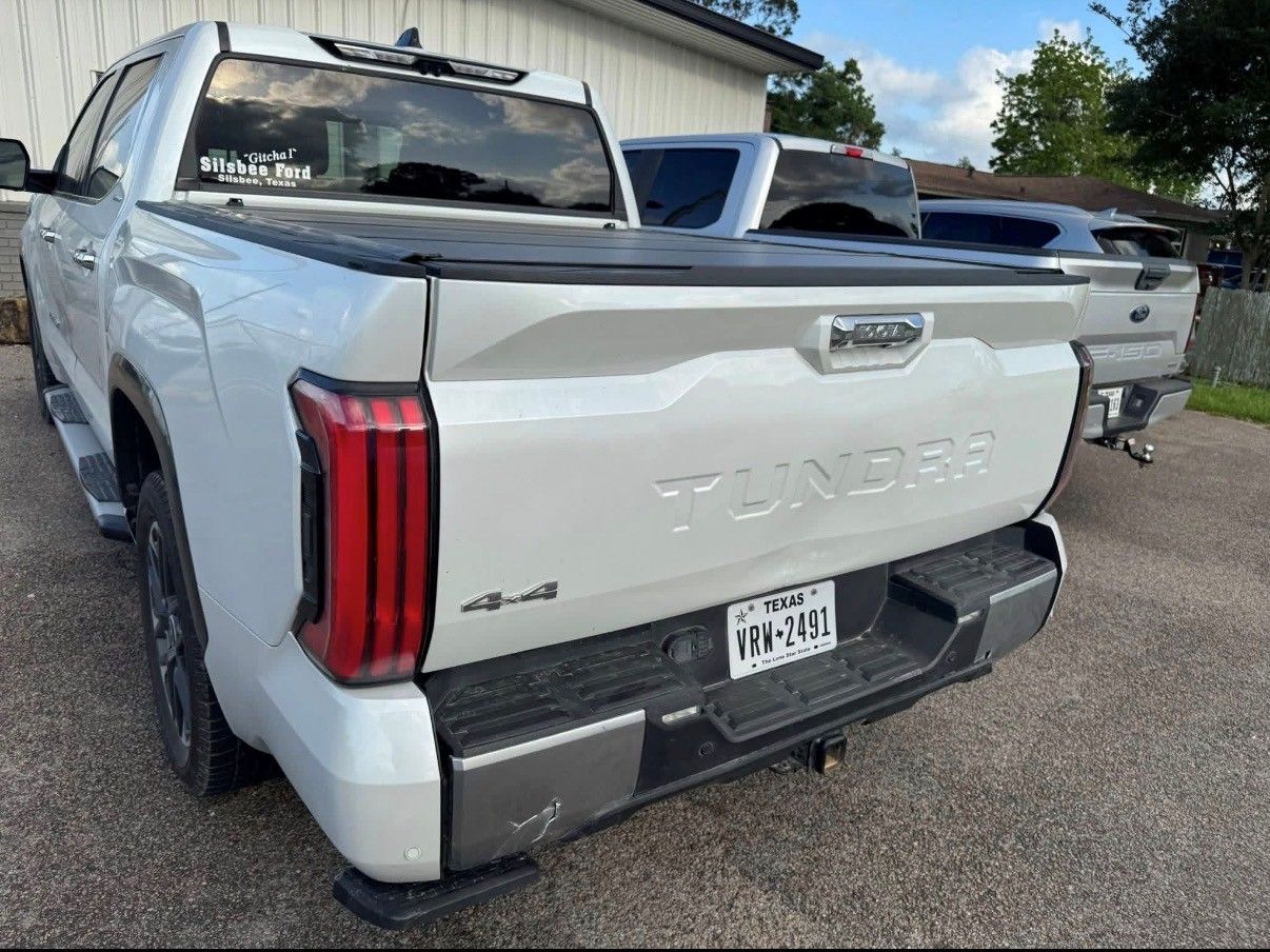 A white Toyota Tundra pickup truck parked outdoors, viewed from the rear, showing the tailgate, taillight, and bumper.