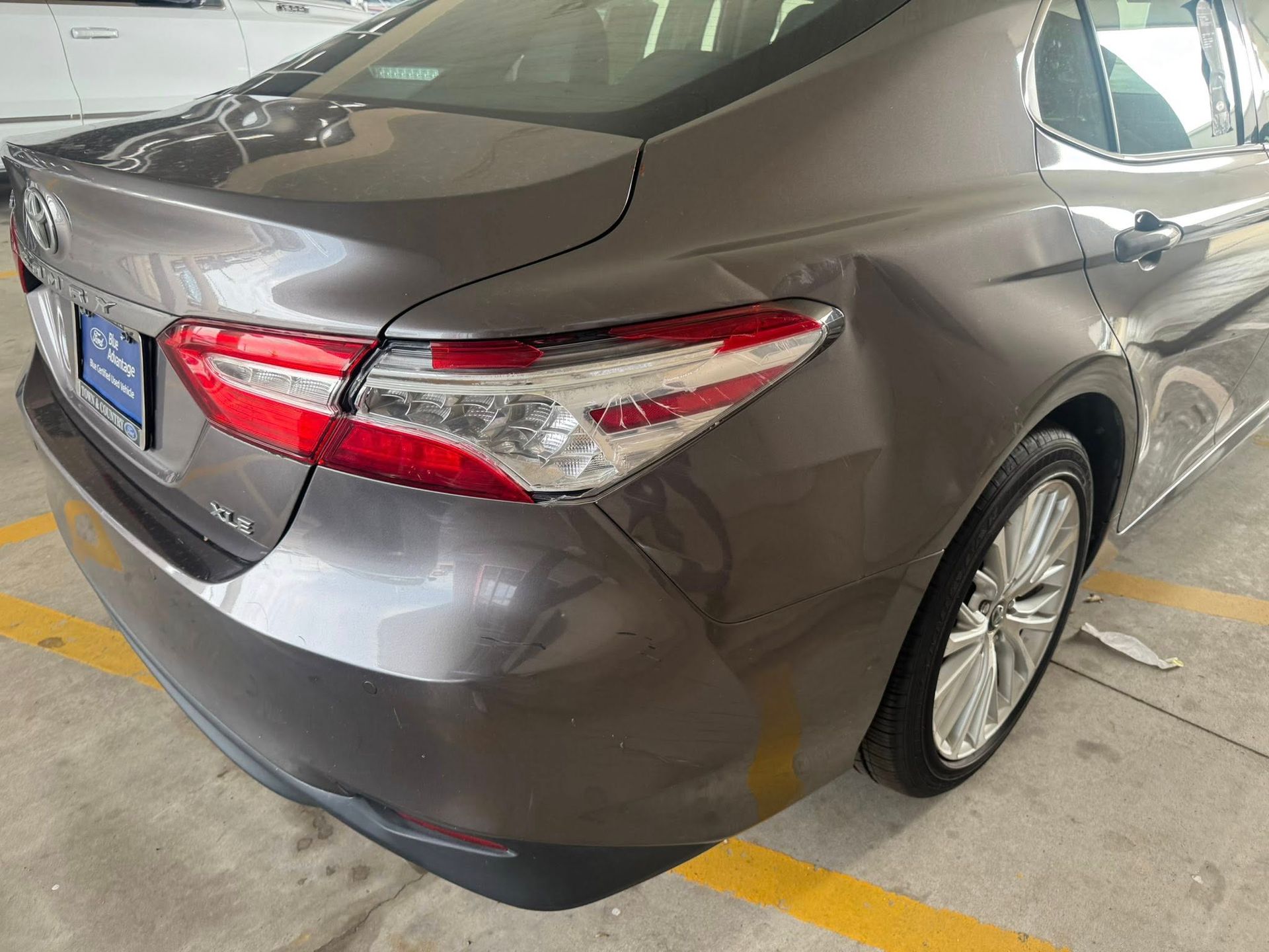A rear view of a gray sedan showing body damage and a dent above the passenger side rear wheel.