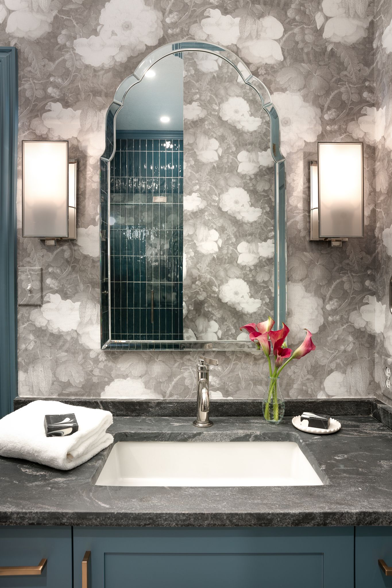 Bathroom vanity with floral wallpaper, ornate mirror, teal cabinet, and silver fixtures