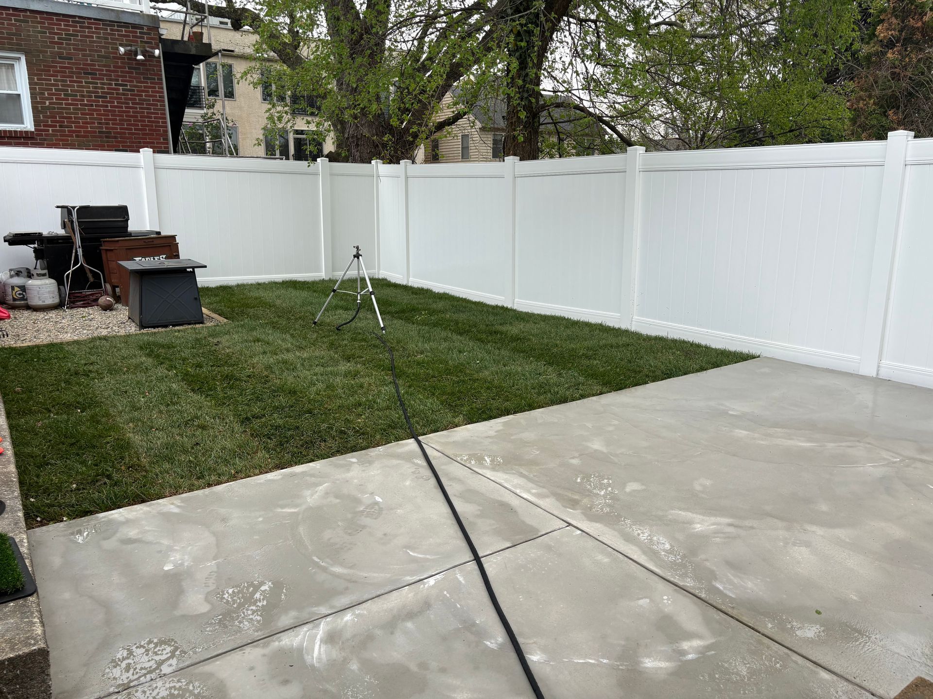 A freshly laid backyard with a concrete patio, a strip of new green grass, and a white vinyl fence.