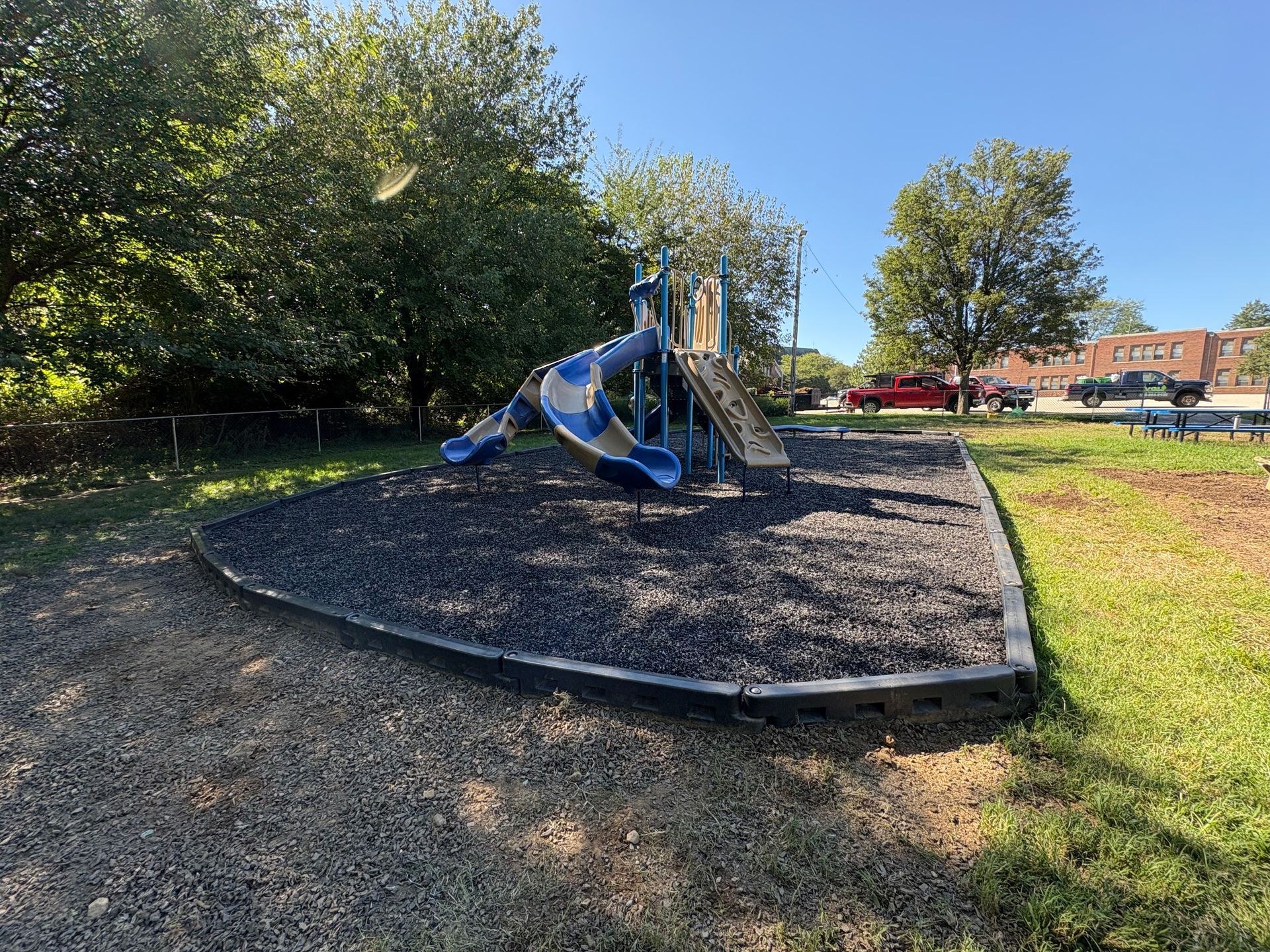 A playground area with a blue and beige spiral slide set on a patch of dark gravel surrounded by a black plastic border.