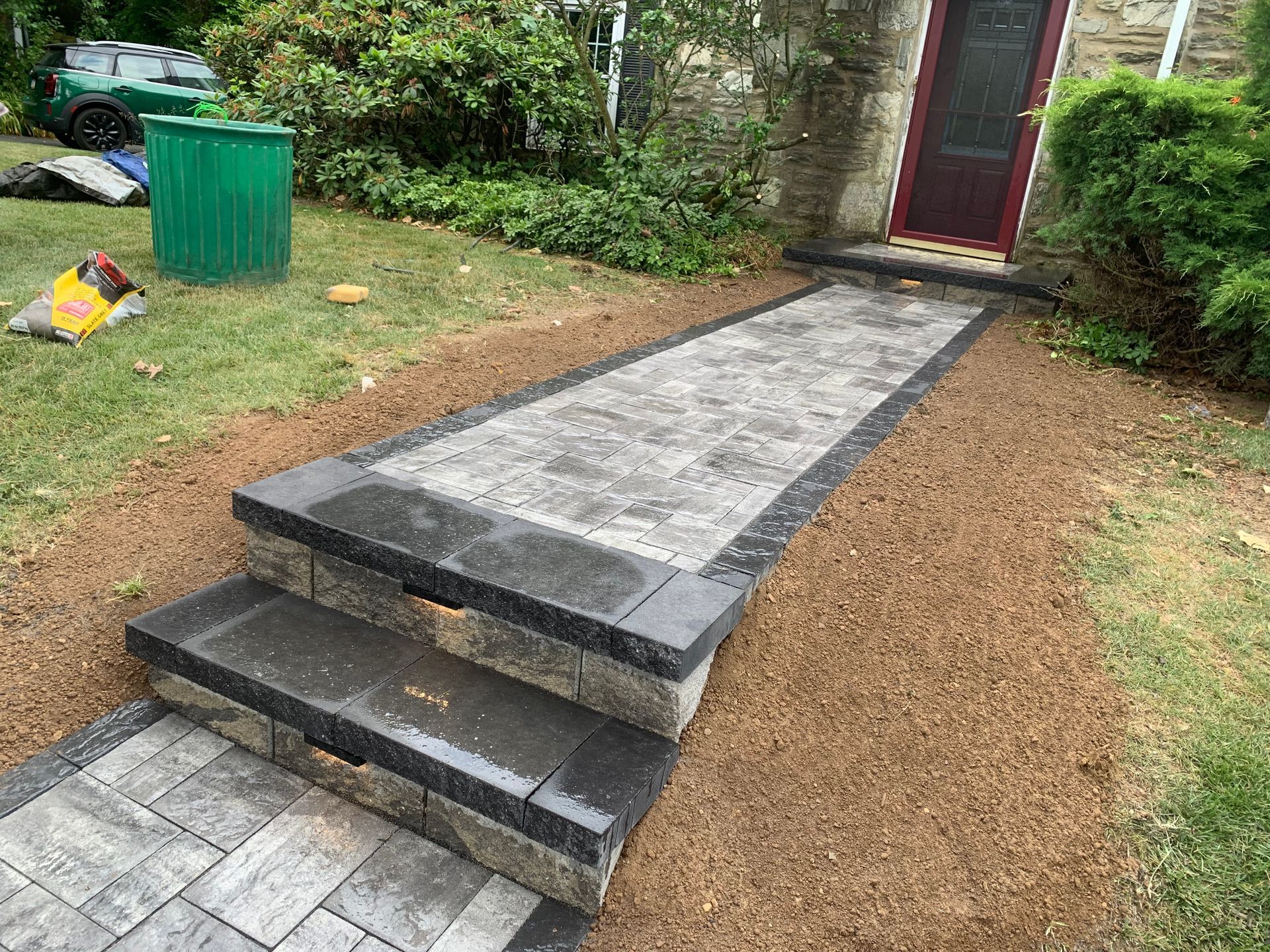 A newly installed paver walkway with two steps leading to a front door, surrounded by mulch and grass.