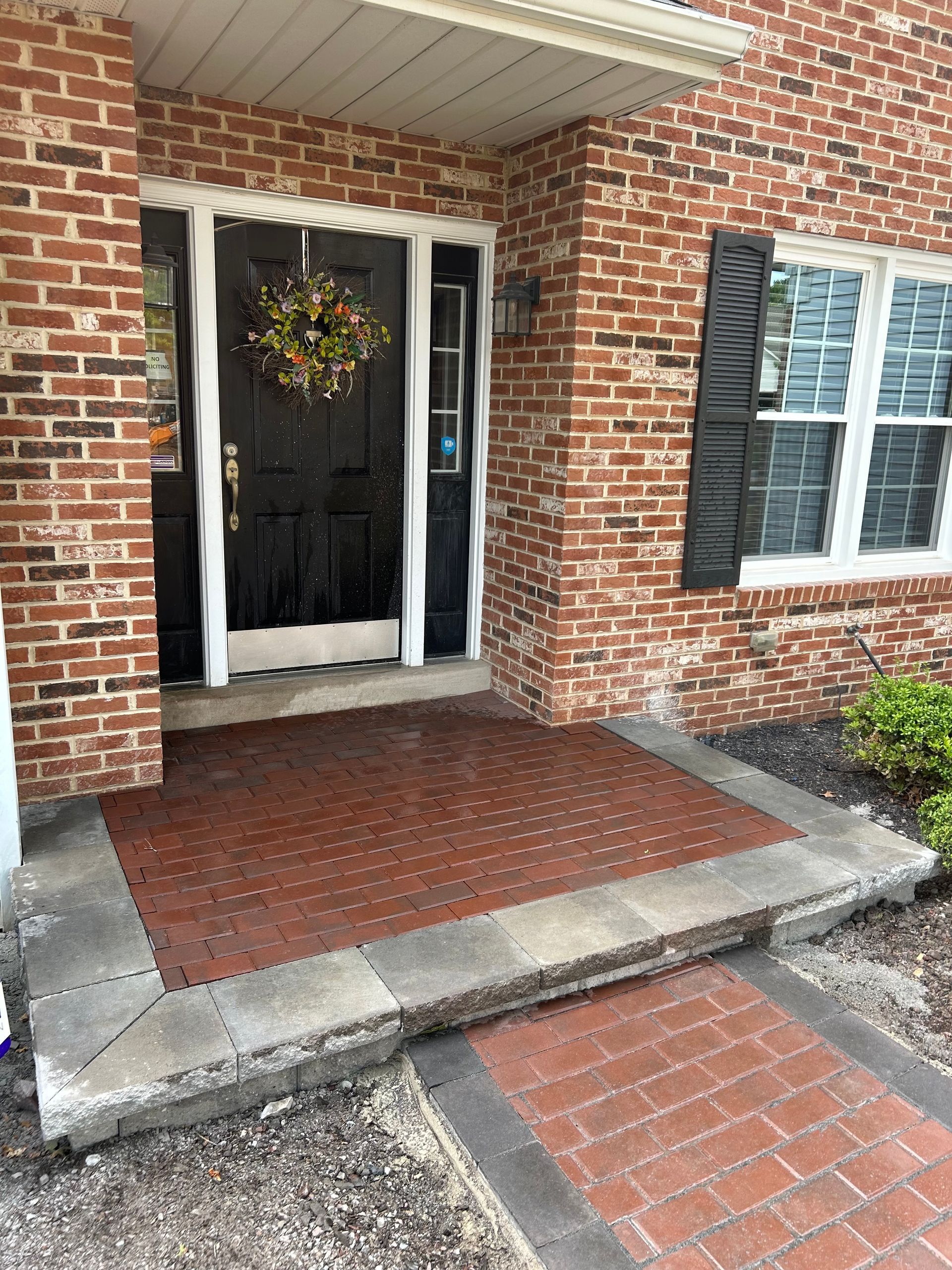 A front porch with a black door, brick exterior, and a stone walkway leading to the entry.