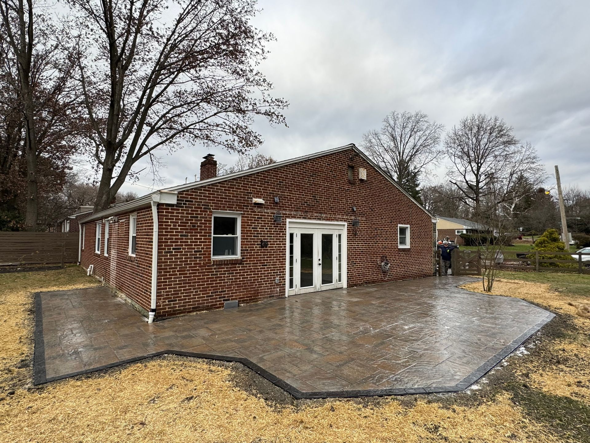 A newly installed stamped concrete patio wraps around the back of a brick house featuring a distinctive, swirling pattern.