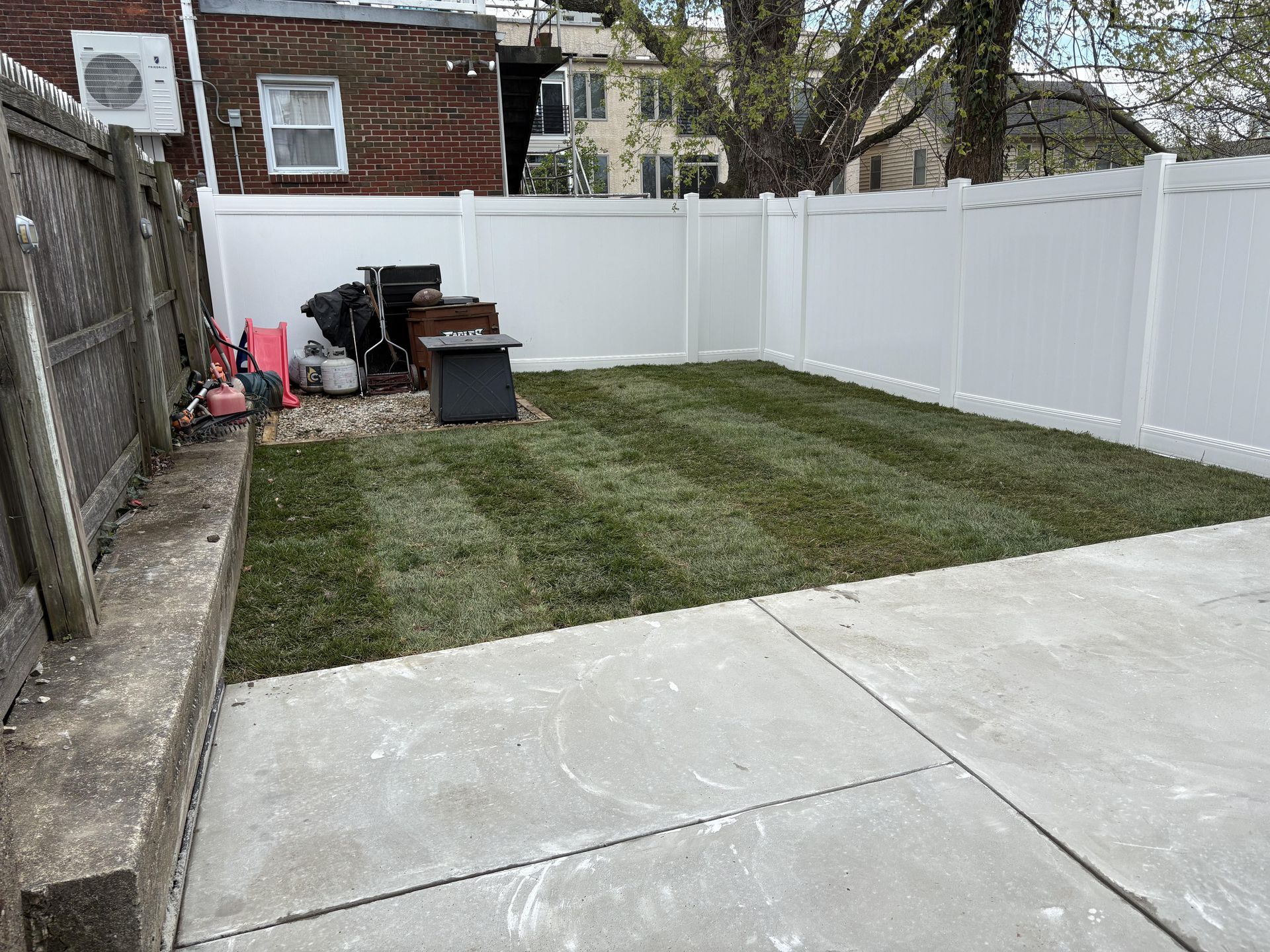 Backyard with concrete patio, white fence, freshly mowed grass, and some equipment.