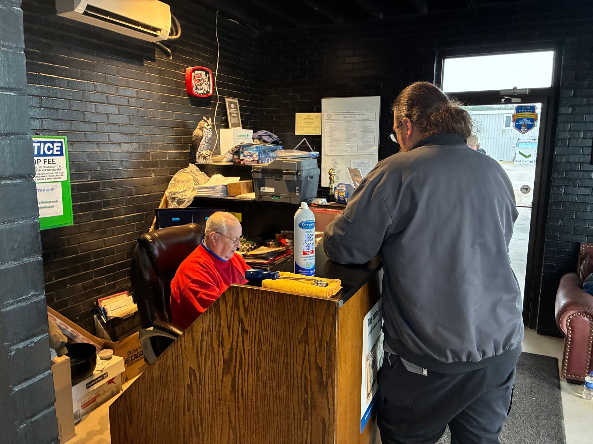 Two men at a dark-walled counter; one standing, one seated behind desk. Interior.