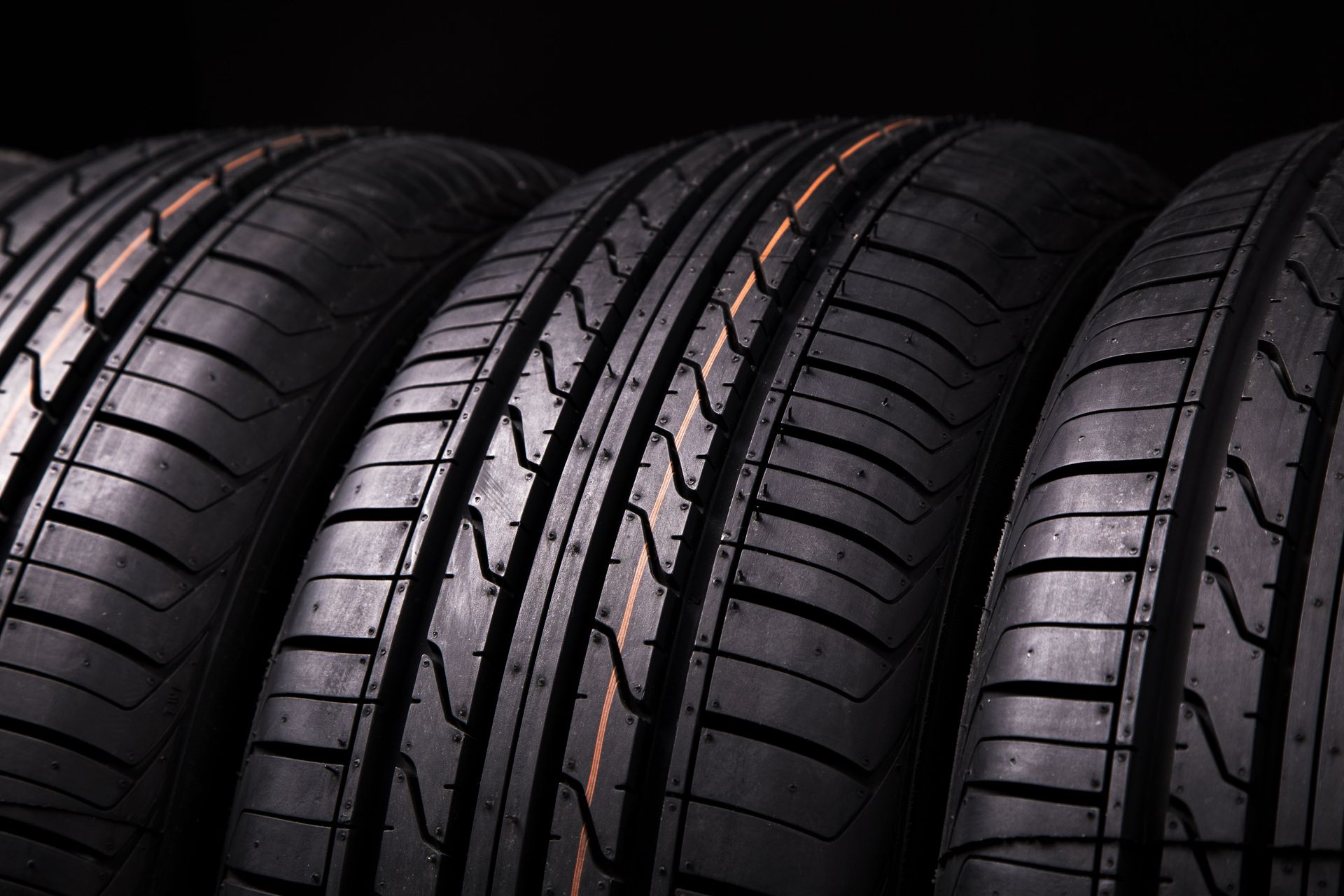 Black car tires in a row, with tread patterns and orange detail.