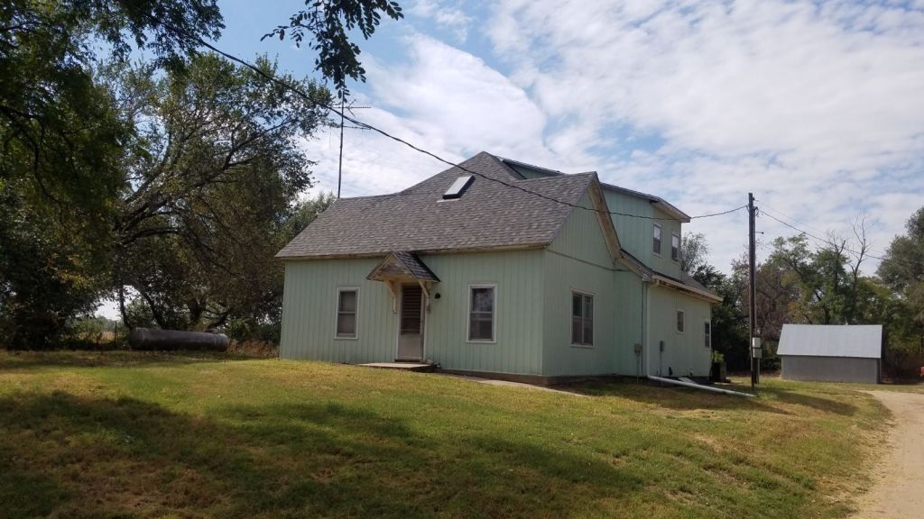 A white house with a gray roof is sitting in the middle of a grassy field.