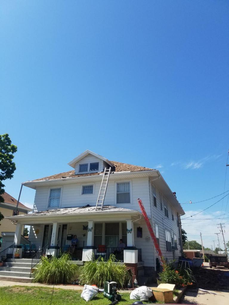A large white house with a red ladder on the roof.