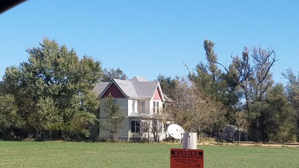 A house with a red roof is in the middle of a field with a warning sign in the foreground.