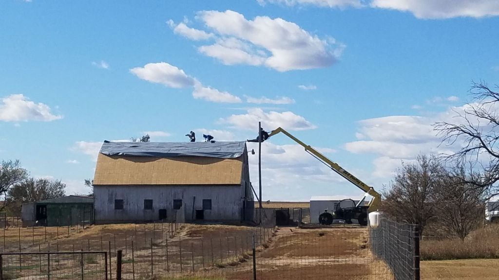 A crane is working on the roof of a barn.