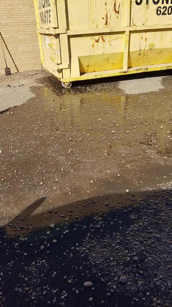 A yellow dumpster is sitting in a puddle of water.