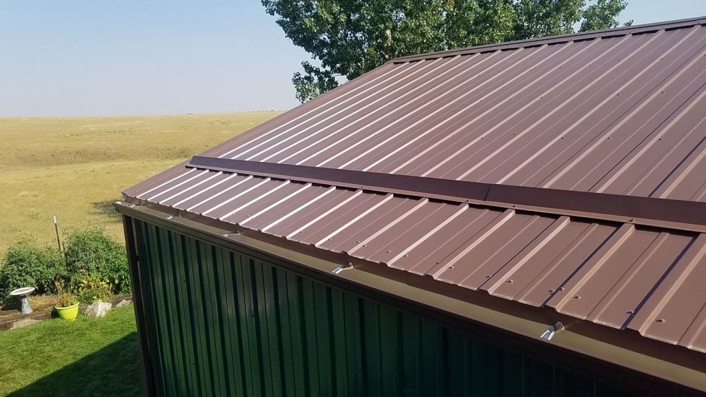 A brown metal roof on a green building with a field in the background.