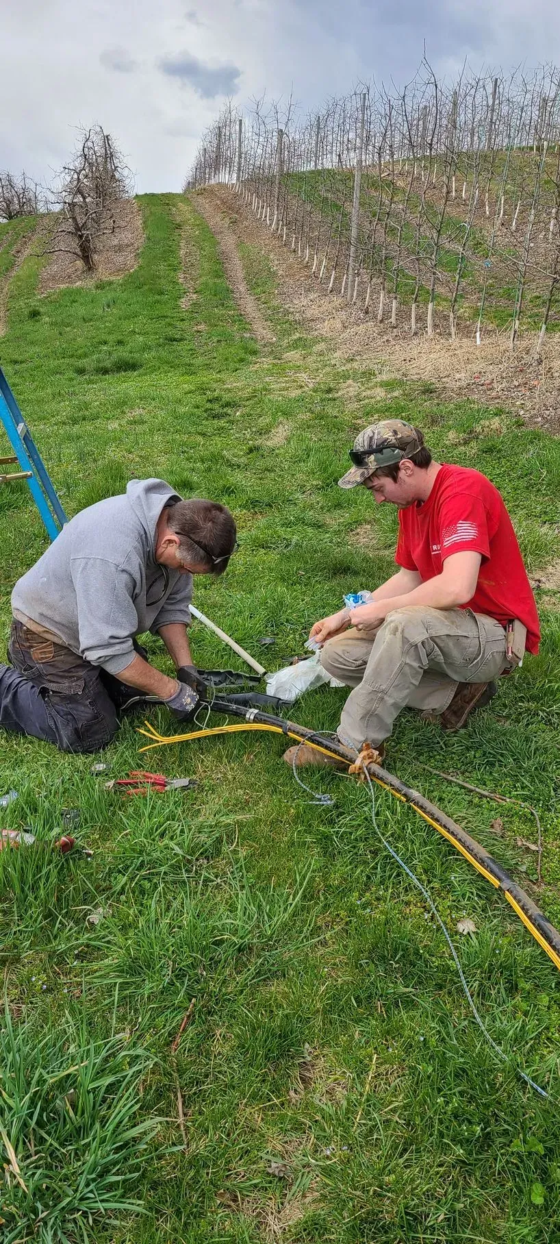 Two men are working on a hose in a field.