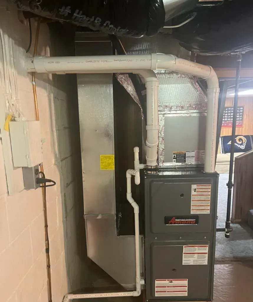 A furnace is sitting in a basement next to a wall.