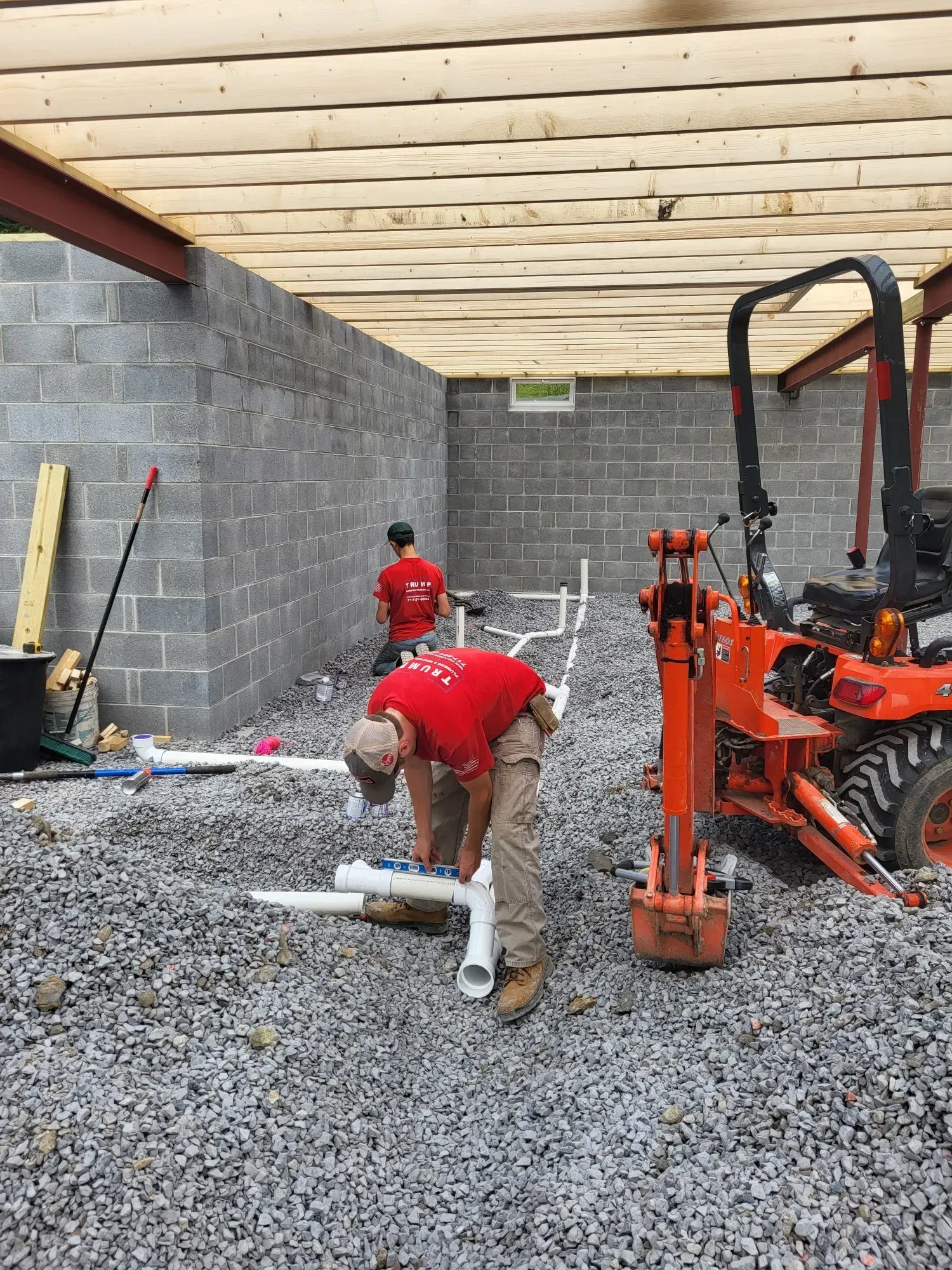 A man in a red shirt is working on pipes in a basement.