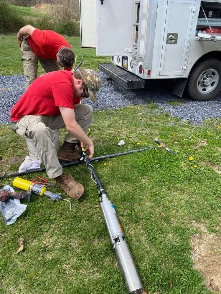 Two men are working on a water pump in front of a truck.