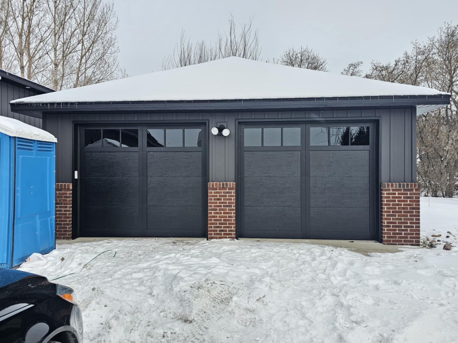 A black garage door is sitting in the snow next to a blue portable toilet.