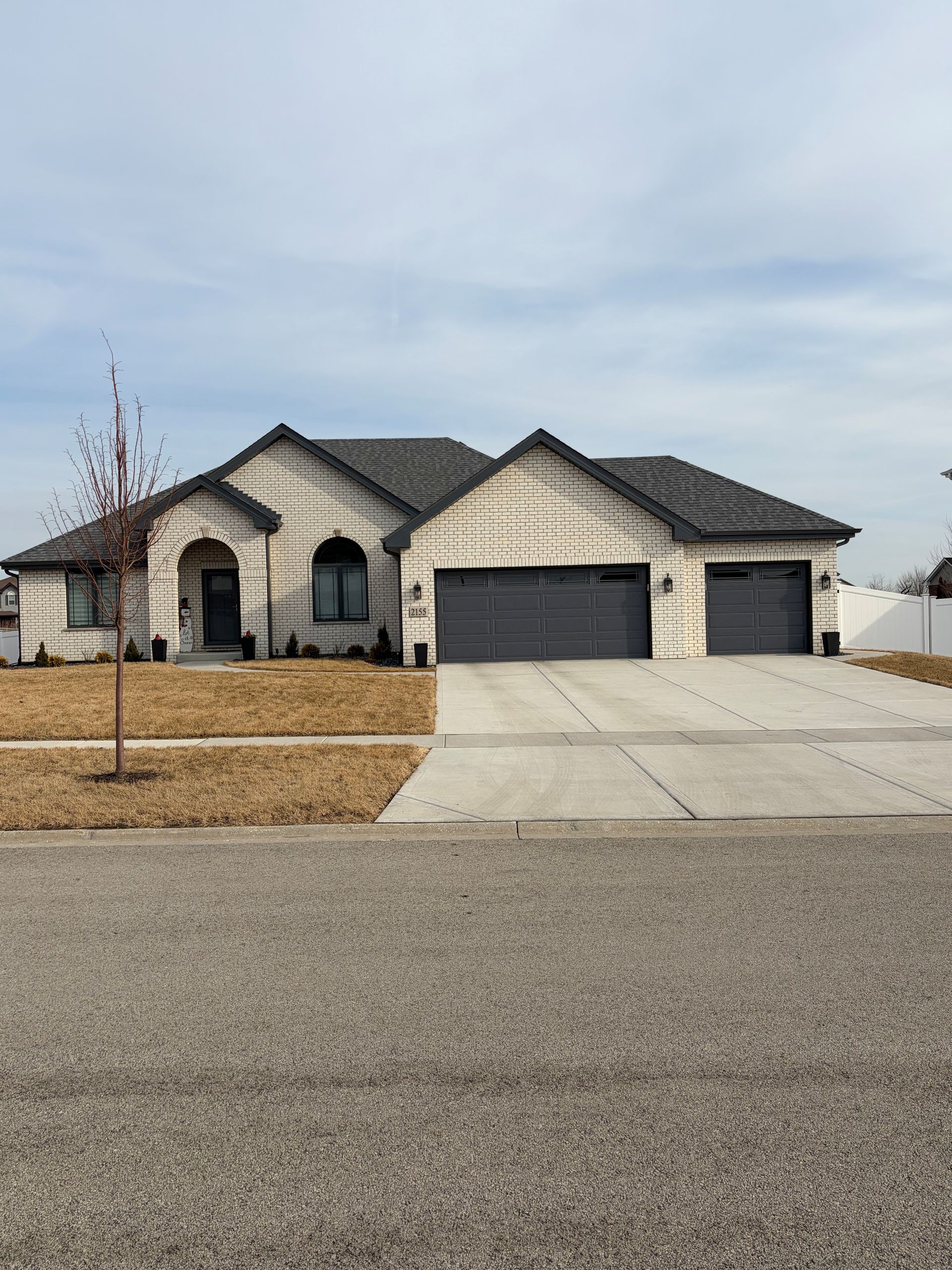 Beige ranch house with grey garage doors and driveway.