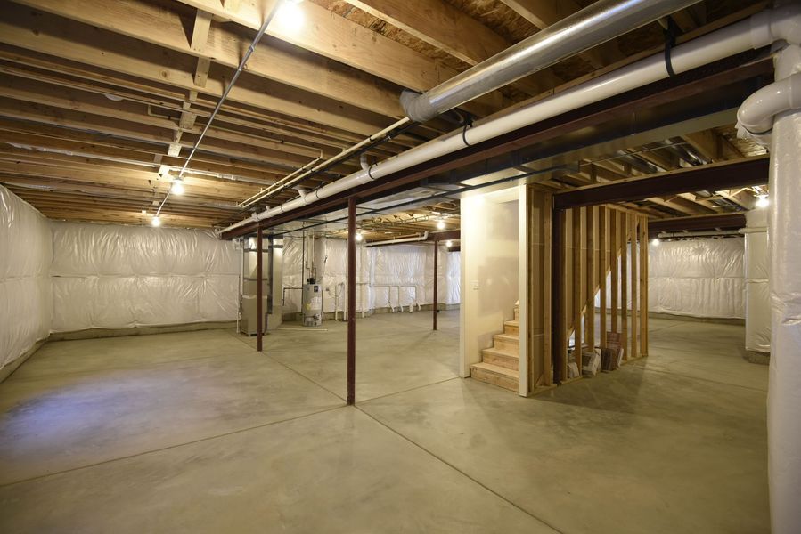 Basement with concrete floor, exposed ceiling beams, ductwork, support posts, and unfinished walls.
