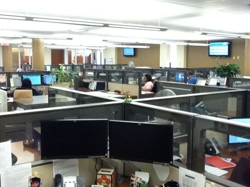 Open office with cubicles, computers, and employees working. Some have two monitors.