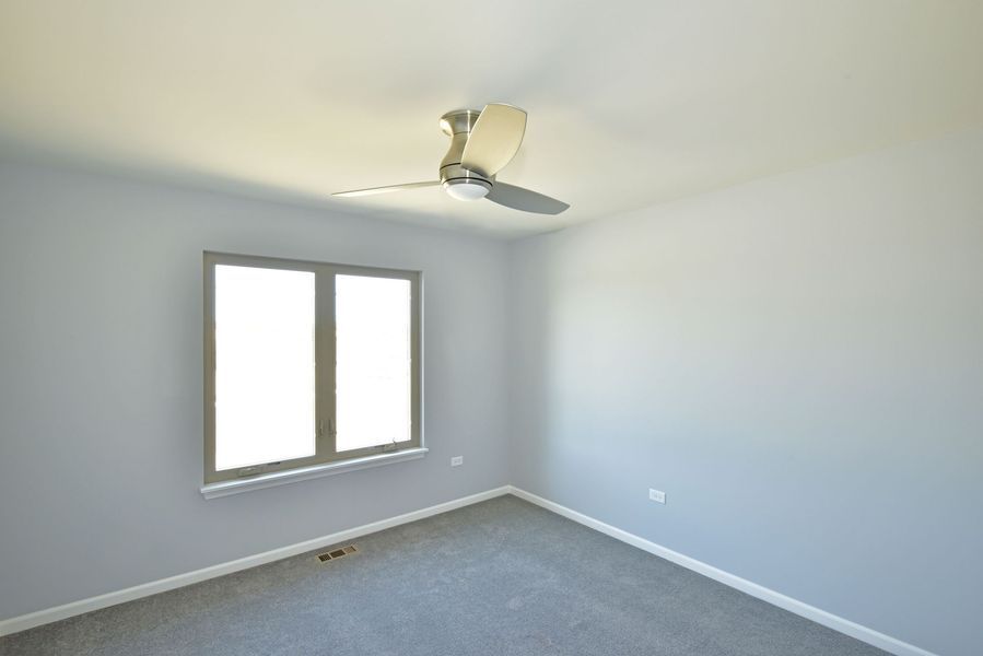 Empty bedroom with gray walls, carpet, window, and ceiling fan.