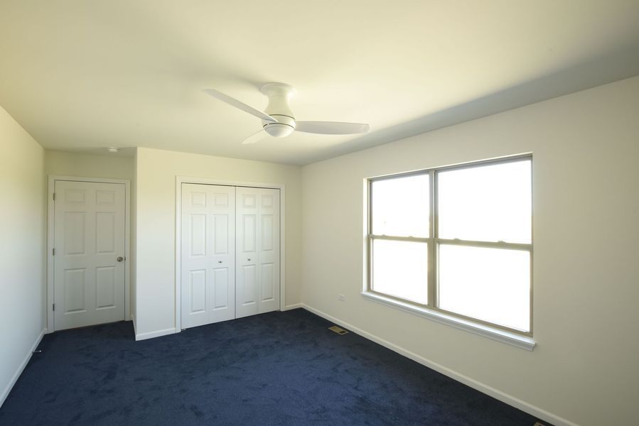 Empty bedroom with blue carpet, white walls, closet, door, window, and ceiling fan.