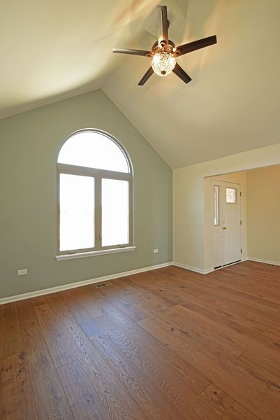 Empty room with arched window, ceiling fan, hardwood floors, and a white door.