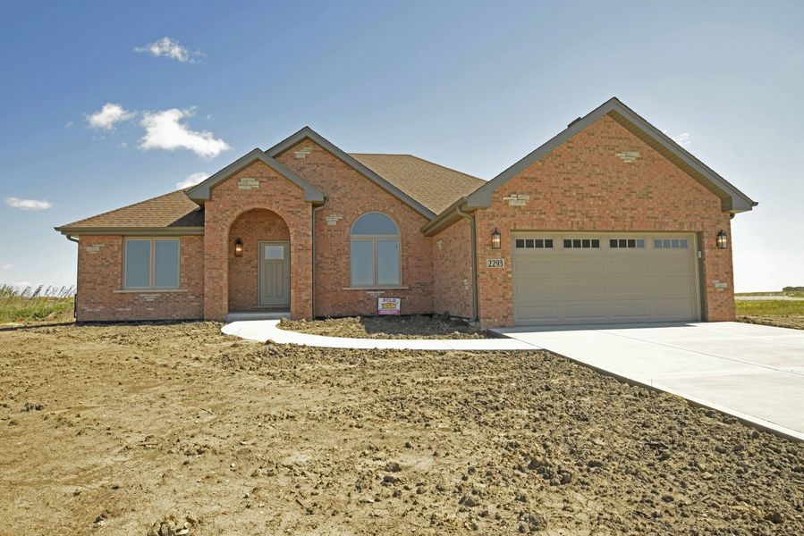 Brick ranch home with a two-car garage, on a bare lot under a blue sky.