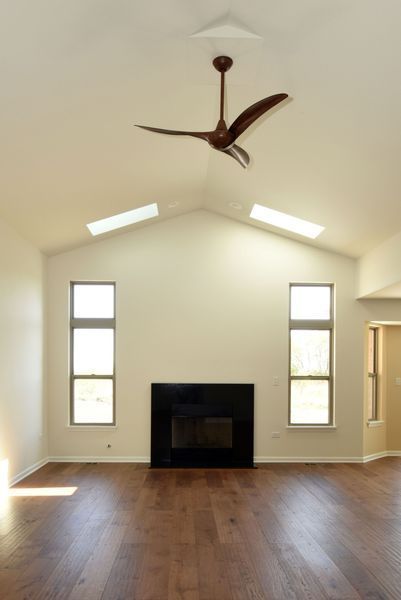 Living room with fireplace, windows, hardwood floor, and a brown ceiling fan.