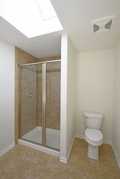 Bathroom with shower and toilet, beige walls and floor, skylight.