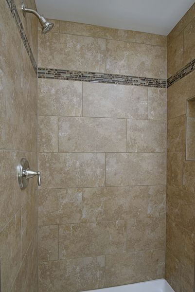 Tiled shower stall with a shower head, faucet, and decorative horizontal stripe.