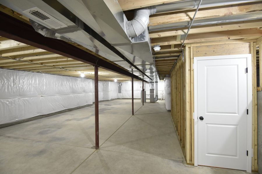 Unfinished basement with concrete floor, insulation, support beams, ductwork, and white door.