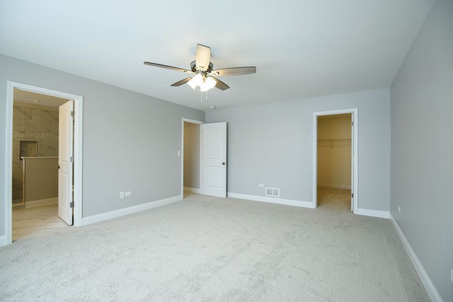 Spacious gray bedroom with carpet, three doorways, and a ceiling fan.